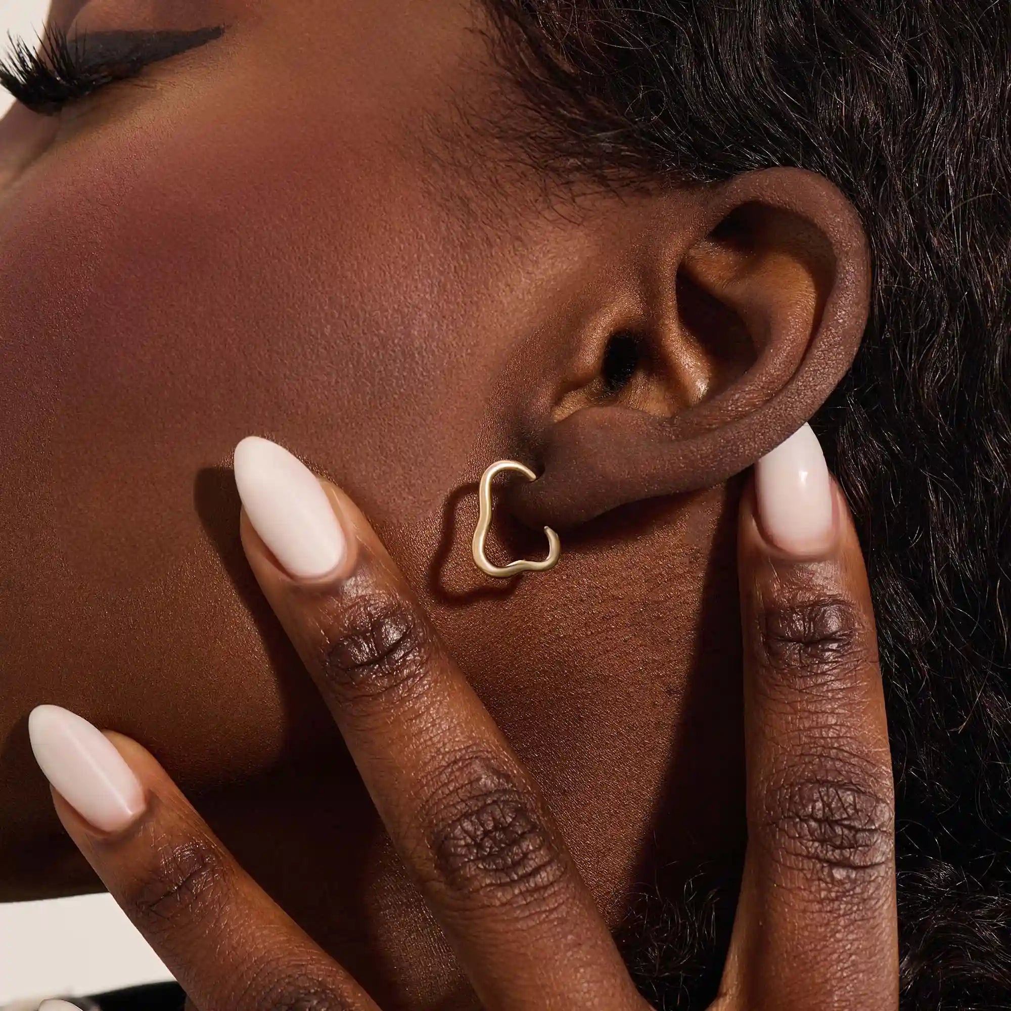 Close-up of a model wearing a 14k solid yellow gold abstract hoop stud earring with a modern sculptural design.
