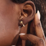 Close-up of a model wearing a 14k solid yellow gold arrow stud earring, showing the sparkle of moissanite stones in the arrowhead.
