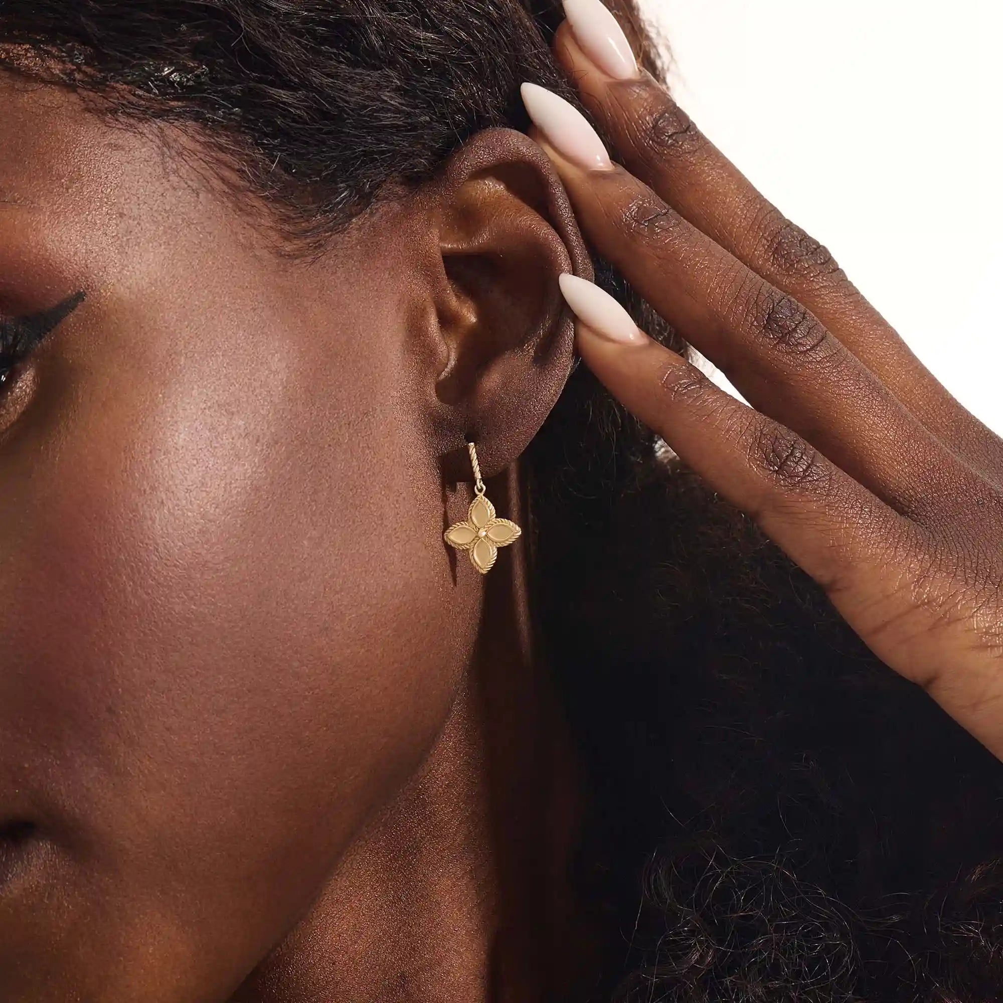 Close-up of a model wearing a 14k solid yellow gold dangle clover stud earring with a twisted post and a polished floral drop.
