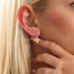 Close-up of a model wearing a 14k solid yellow gold dangle clover stud earring with a twisted post and a polished floral drop.
