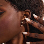 Close-up of a model wearing a 14k solid yellow gold dangling arrow stud earring with sparkling moissanites in bezel and pavé settings.
