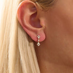Close-up of a model wearing a 14k solid yellow gold dangling arrow stud earring with sparkling moissanites in bezel and pavé settings.
