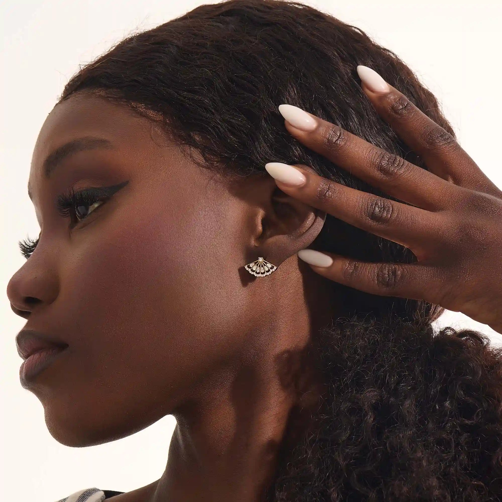 Close-up of a model wearing a 14k solid yellow gold fan stud earring, the moissanite stones catching the light for a glamorous, art deco-inspired look.
