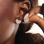 Close-up of a model wearing a 14k solid yellow gold mixed-cut heart stud earring, showcasing the sparkle of baguette and round white moissanite stones.
