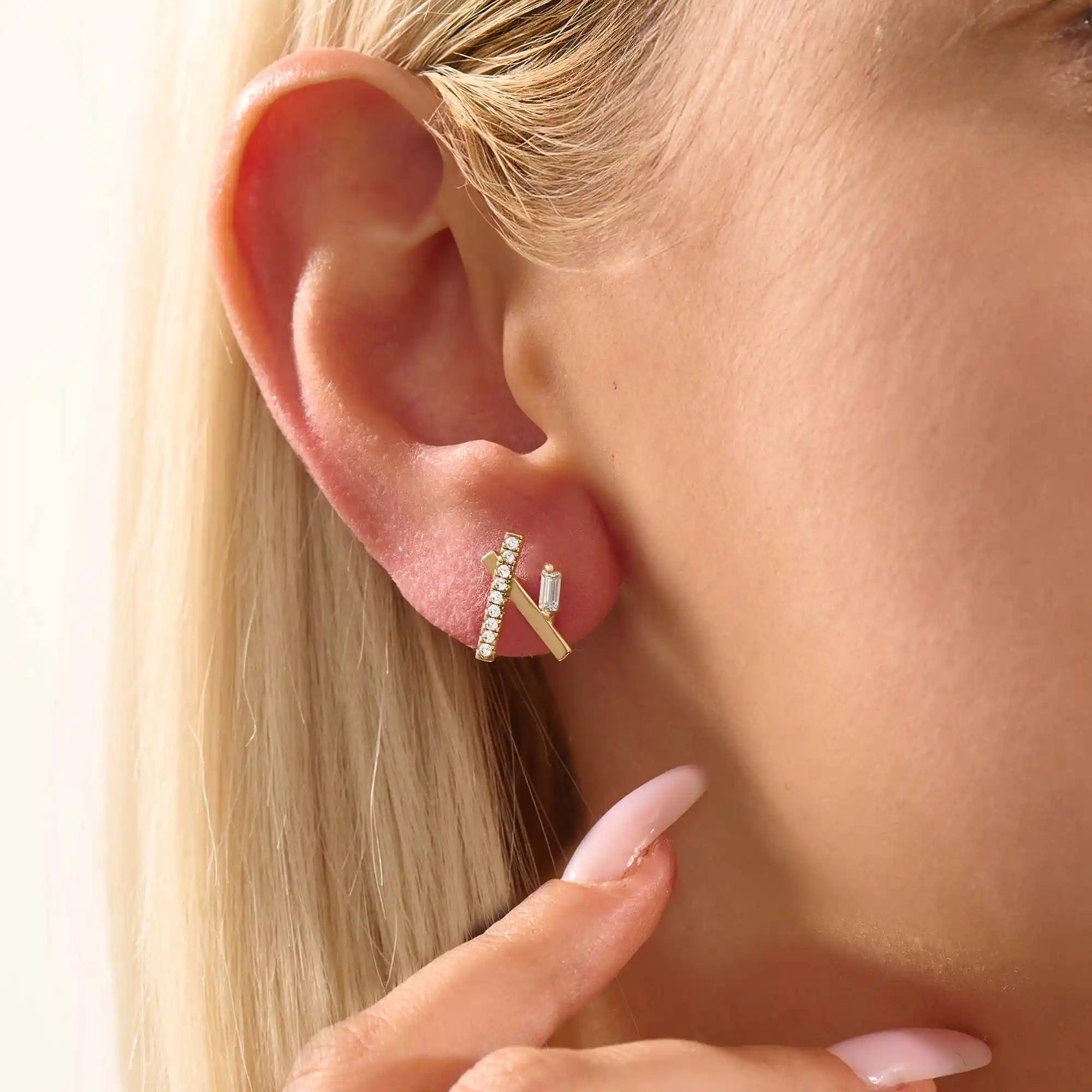 Close-up of a model wearing a 14k yellow gold bar stud with moissanite row and baguette-cut accent stone.
