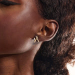 Close-up of a model wearing a 14k yellow gold bar stud with moissanite row and baguette-cut accent stone.
