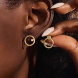 Close-up of a model wearing a 14k yellow gold karma circle stud with a single bezel-set moissanite detail.
