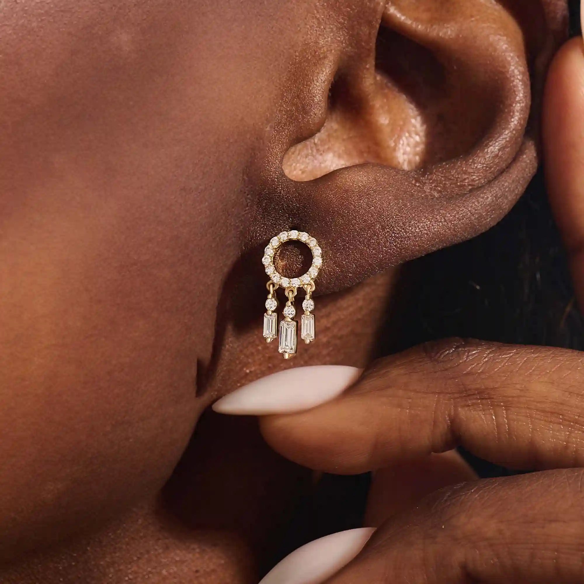 Close-up of a model wearing a 14k yellow gold pavé-set circle stud earring with three moissanite drop charms.
