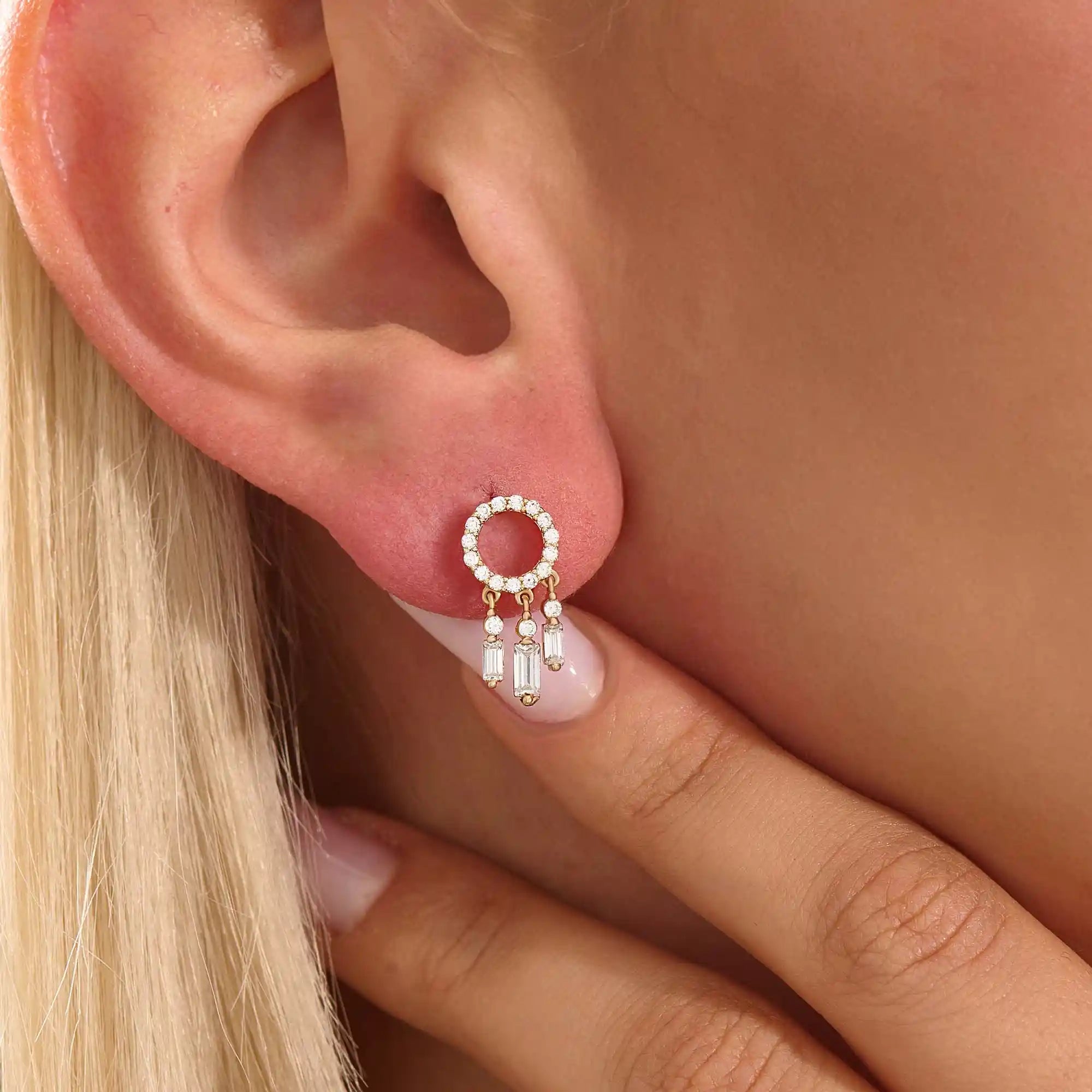 Close-up of a model wearing a 14k yellow gold pavé-set circle stud earring with three moissanite drop charms.
