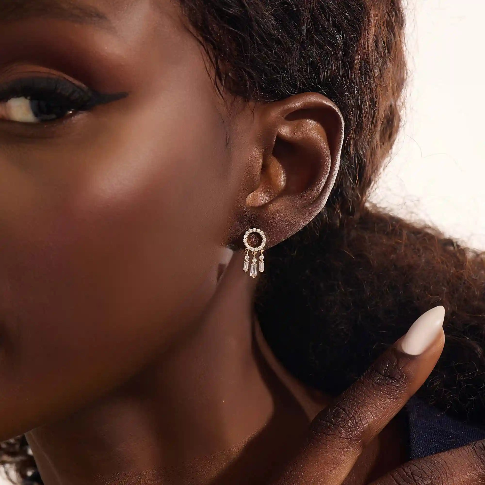 Close-up of a model wearing a 14k yellow gold pavé-set circle stud earring with three moissanite drop charms.
