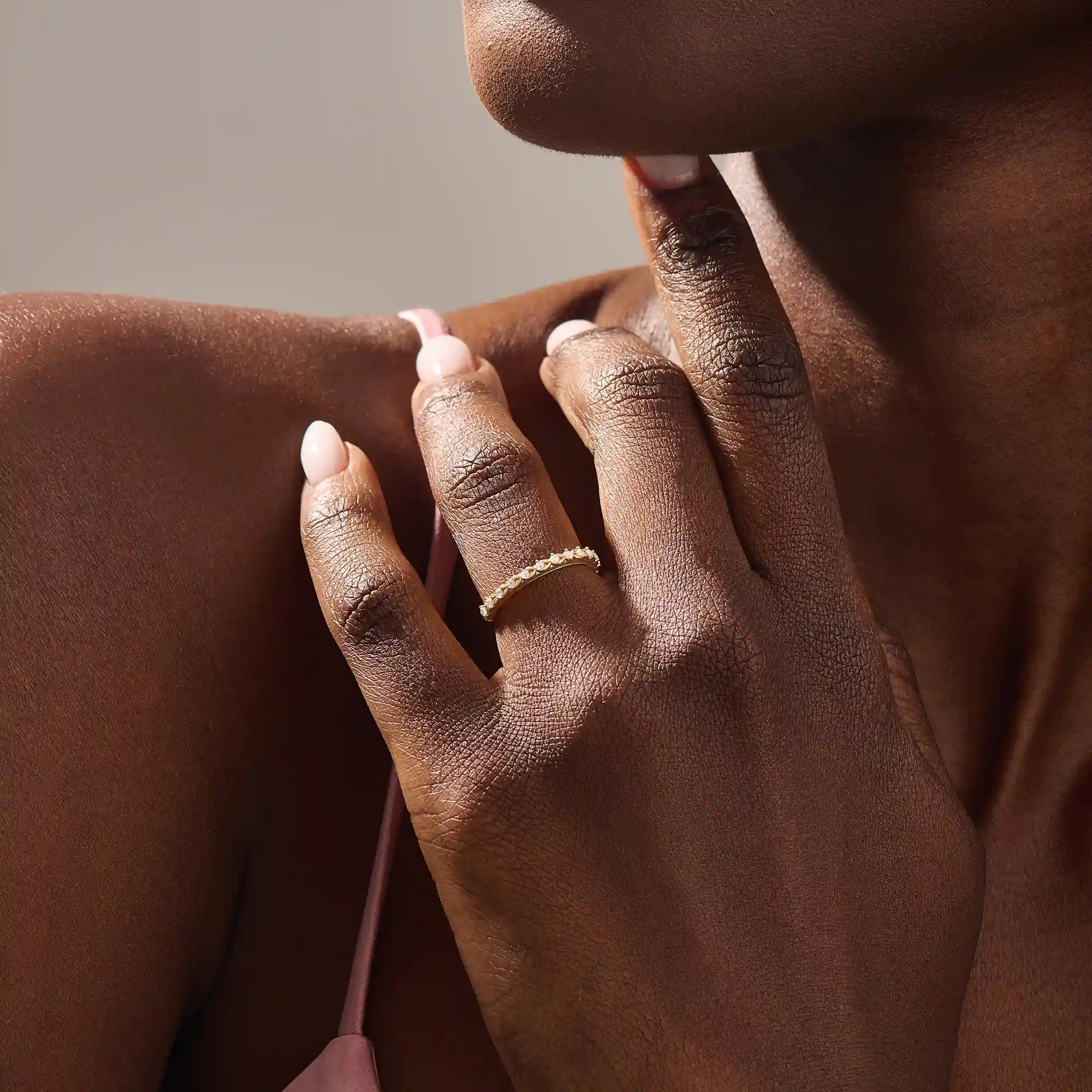 Close-up of a woman’s hand wearing a 14k solid yellow gold eternity band with round brilliant cut moissanite stones in leaf motif prong settings, minimal and elegant bridal jewelry