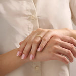 Close-up of a woman’s hand wearing a 14k solid yellow gold eternity band with round brilliant cut moissanite stones in leaf motif prong settings, minimal and elegant bridal jewelry