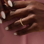 Close-up of a woman’s hand wearing a 14k solid yellow gold eternity band with round brilliant cut moissanite stones in leaf motif prong settings, minimal and elegant bridal jewelry