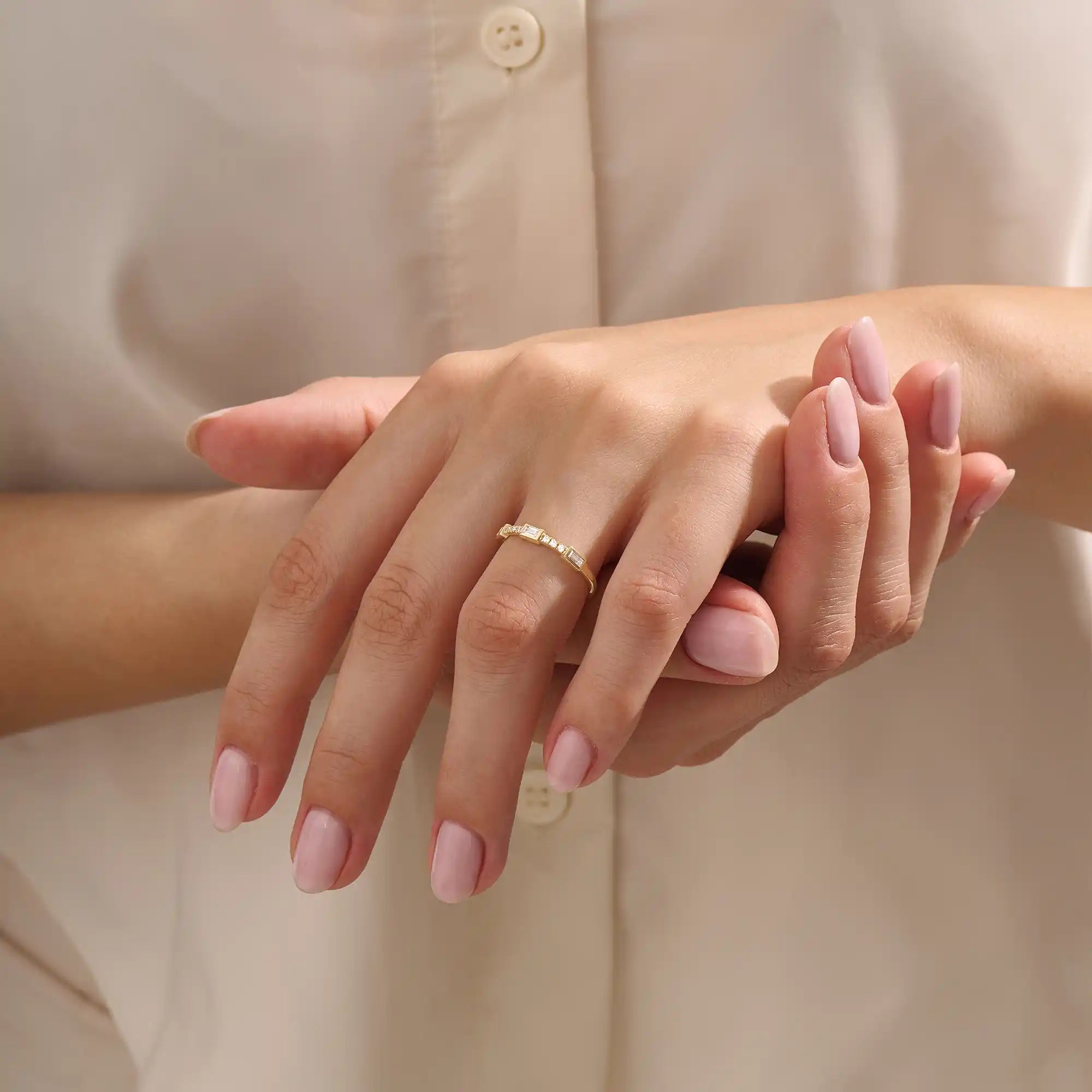 Close-up of a woman wearing a 14k solid yellow gold band with a baguette cut moissanite center stone and round brilliant cut moissanite accents, minimal and modern fine jewelry
