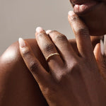Close-up of a woman wearing a 14k solid yellow gold band with a baguette cut moissanite center stone and round brilliant cut moissanite accents, minimal and modern fine jewelry
