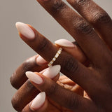 Close-up of a woman wearing a 14k solid yellow gold band with alternating baguette cut and round brilliant cut moissanite stones in a bezel setting, minimal and modern wedding or stacking ring
