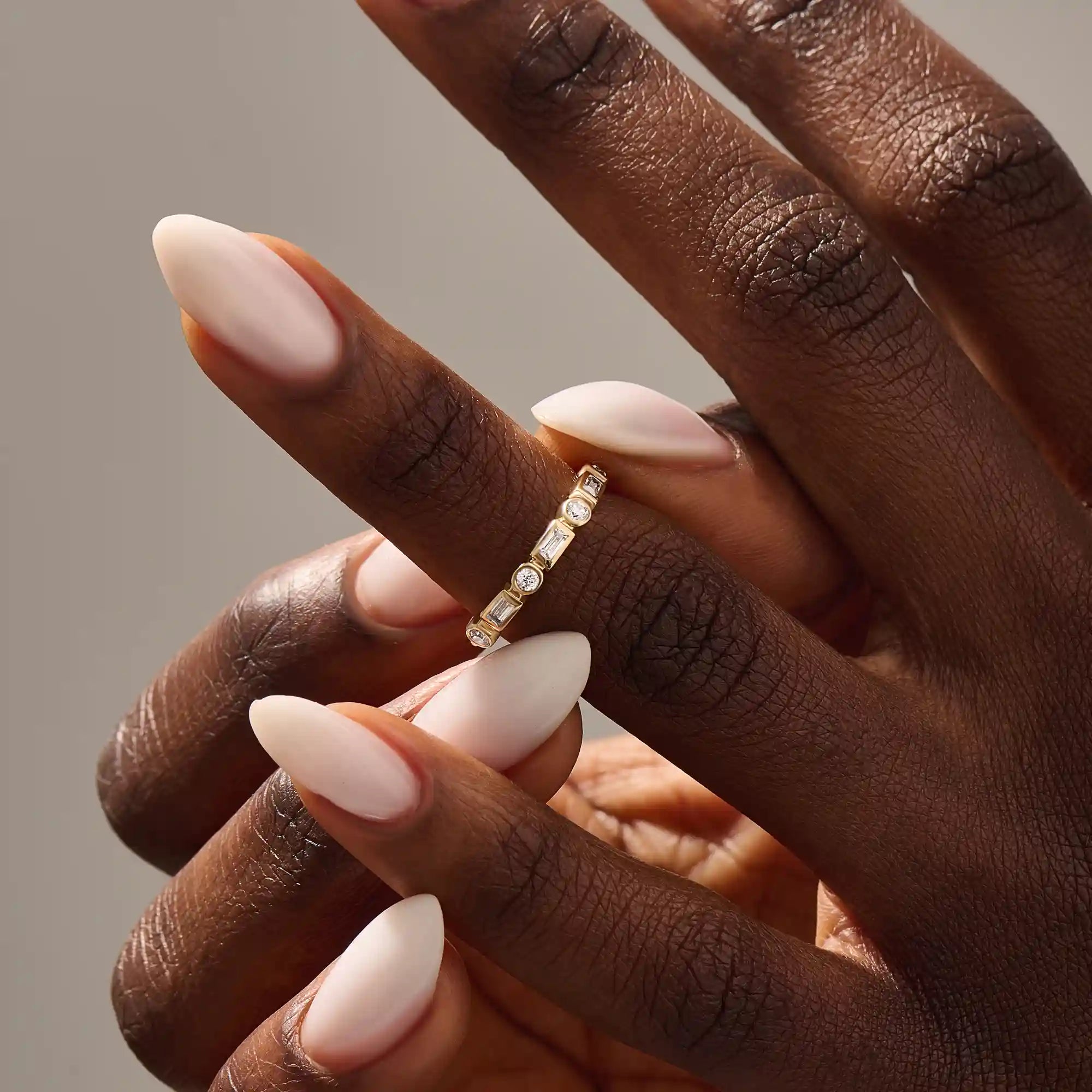 Close-up of a woman wearing a 14k solid yellow gold band with alternating baguette cut and round brilliant cut moissanite stones in a bezel setting, minimal and modern wedding or stacking ring
