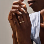 Close-up of a woman wearing a 14k solid yellow gold band with alternating baguette cut and round brilliant cut moissanite stones in a bezel setting, minimal and modern wedding or stacking ring
