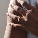 Close-up of a woman wearing a 14k solid yellow gold band with five round brilliant cut moissanite stones in a prong setting and engraved shank detail, sophisticated wedding or anniversary ring
