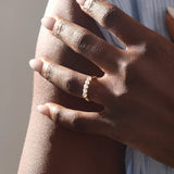 Close-up of a woman wearing a 14k solid yellow gold band with five round brilliant cut moissanite stones in a prong setting and engraved shank detail, sophisticated wedding or anniversary ring
