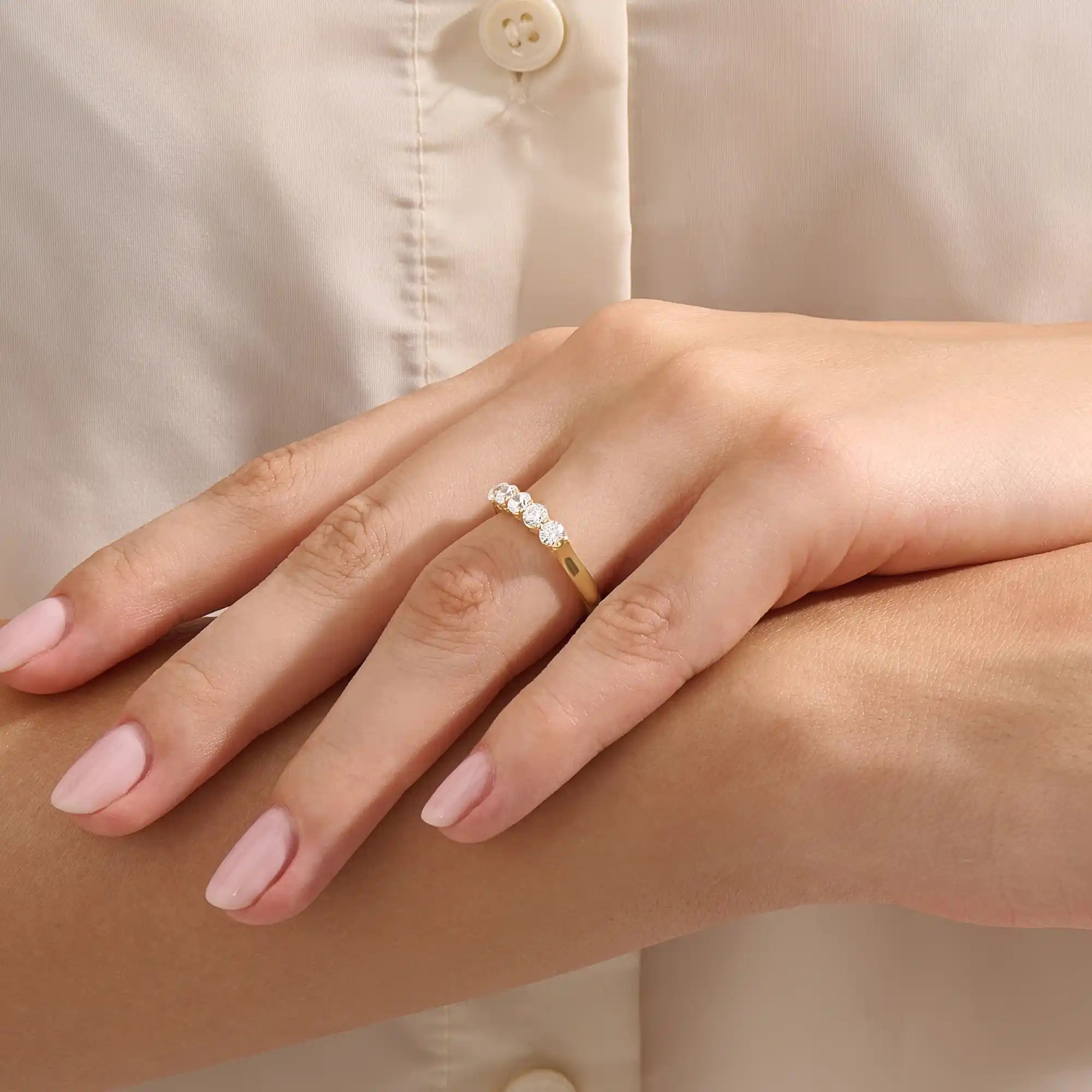 Close-up of a woman wearing a 14k solid yellow gold band with five round brilliant cut moissanite stones in a prong setting and engraved shank detail, sophisticated wedding or anniversary ring
