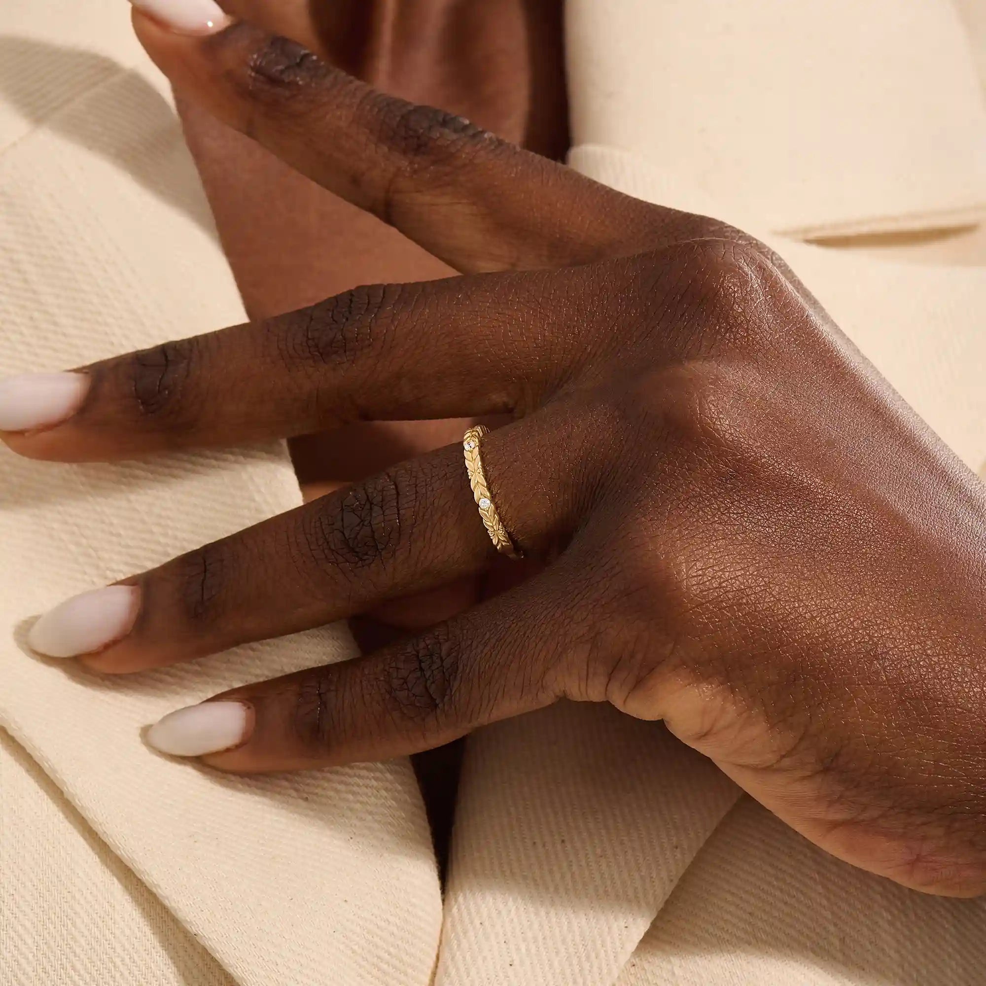 Close-up of a woman wearing a 14k solid yellow gold band with laurel leaf design and bezel set round brilliant cut moissanite stones, elegant and nature-inspired wedding ring
