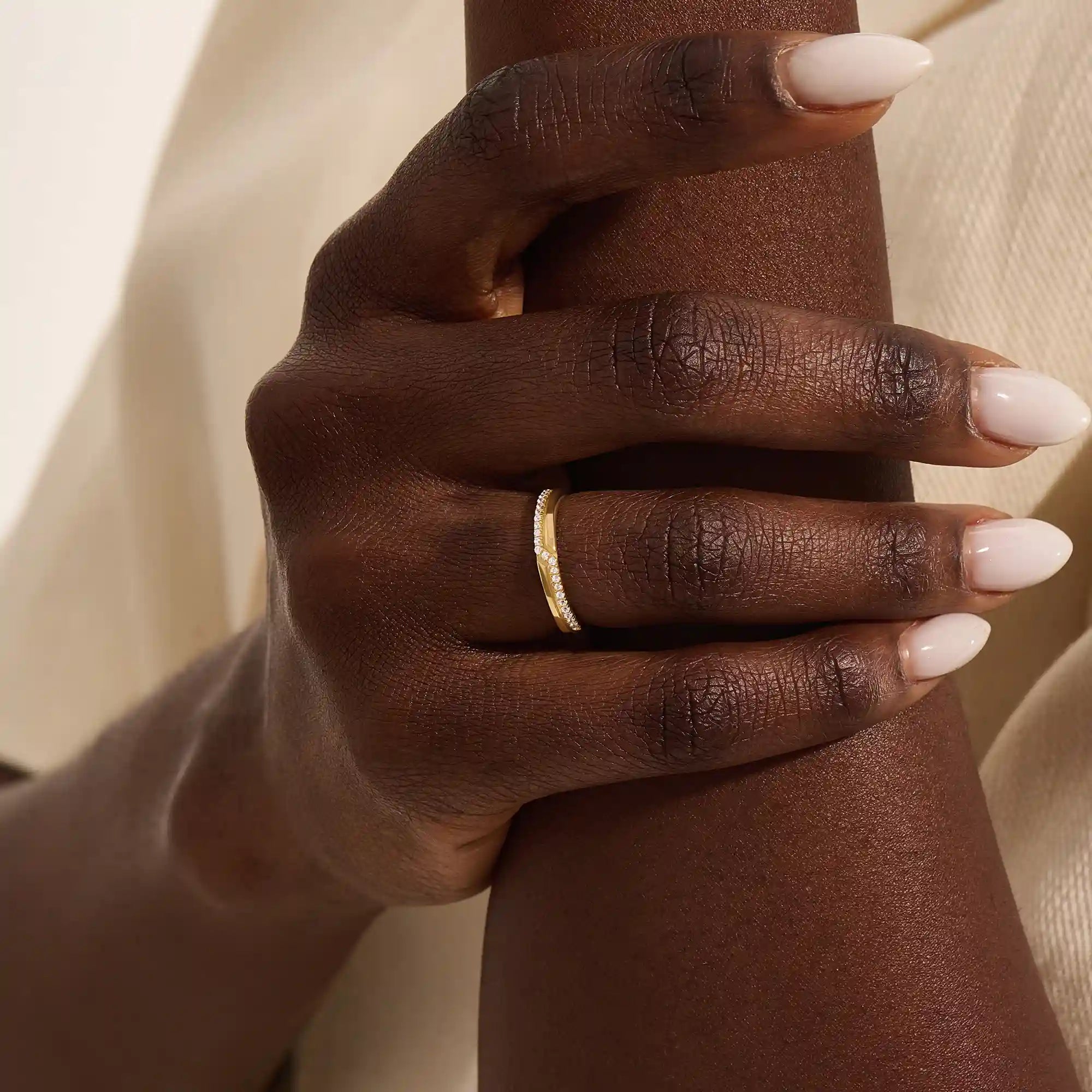 Close-up of a woman wearing a 14k solid yellow gold band with pointed chevron design and pavé set round brilliant cut moissanite stones, minimal and elegant wedding or stacking ring
