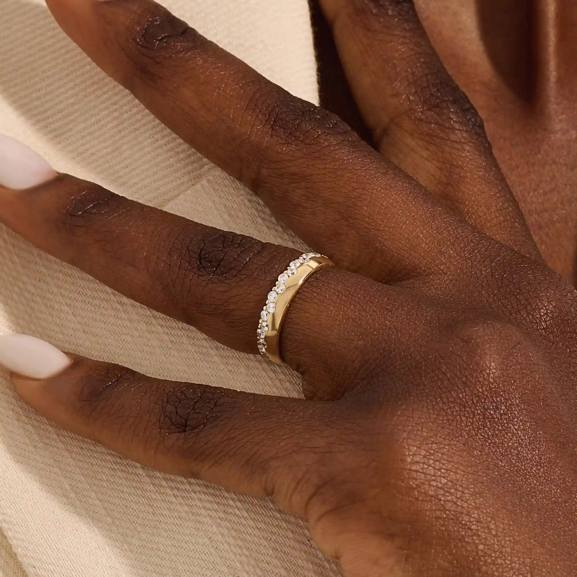 Close-up of a woman wearing a 14k solid yellow gold band with round brilliant cut moissanite stones in a single row and polished bead accents, elegant and timeless wedding jewelry
