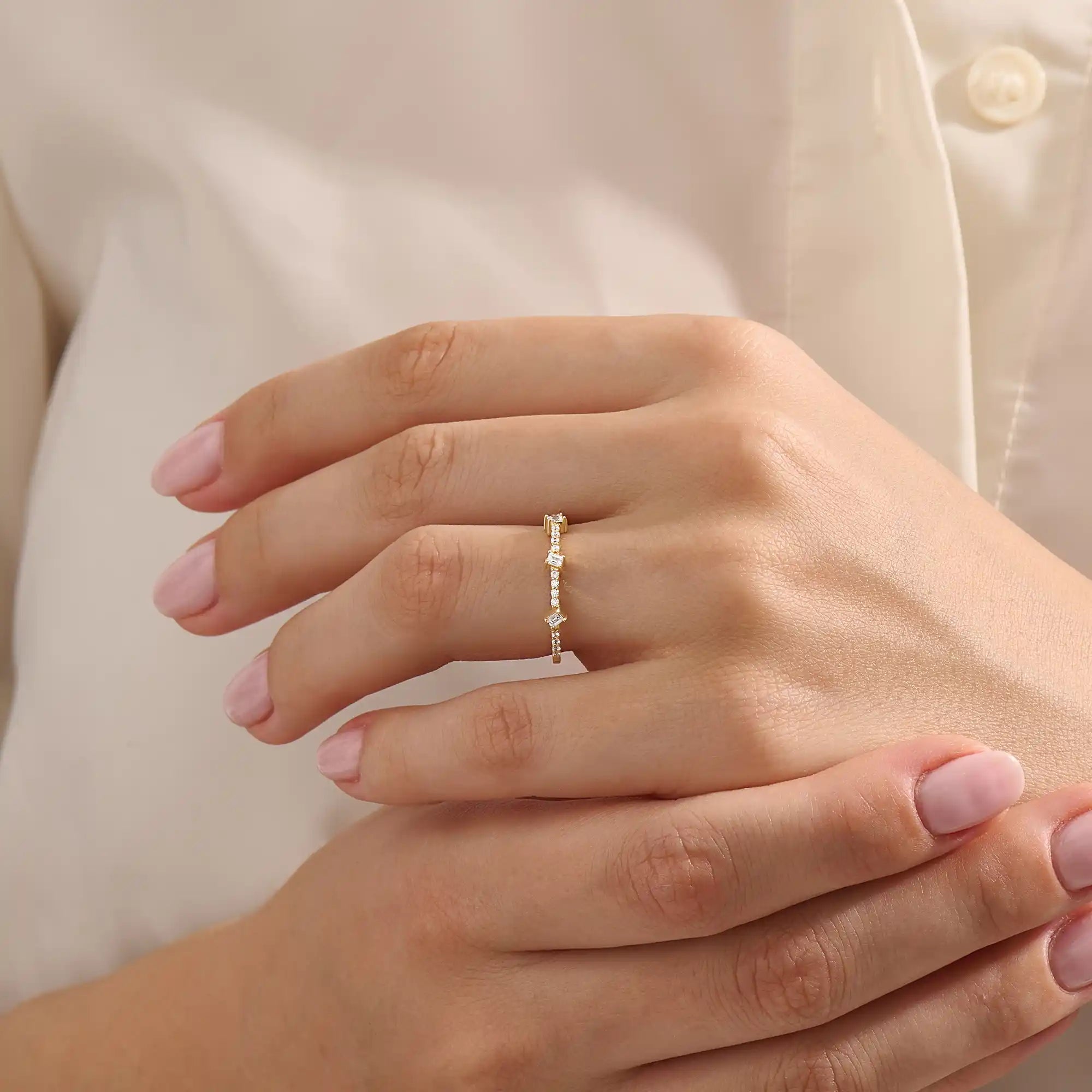Close-up of a woman wearing a 14k solid yellow gold band with three baguette cut moissanite stones and pavé set round moissanite accents, stylish and modern wedding or stacking ring
