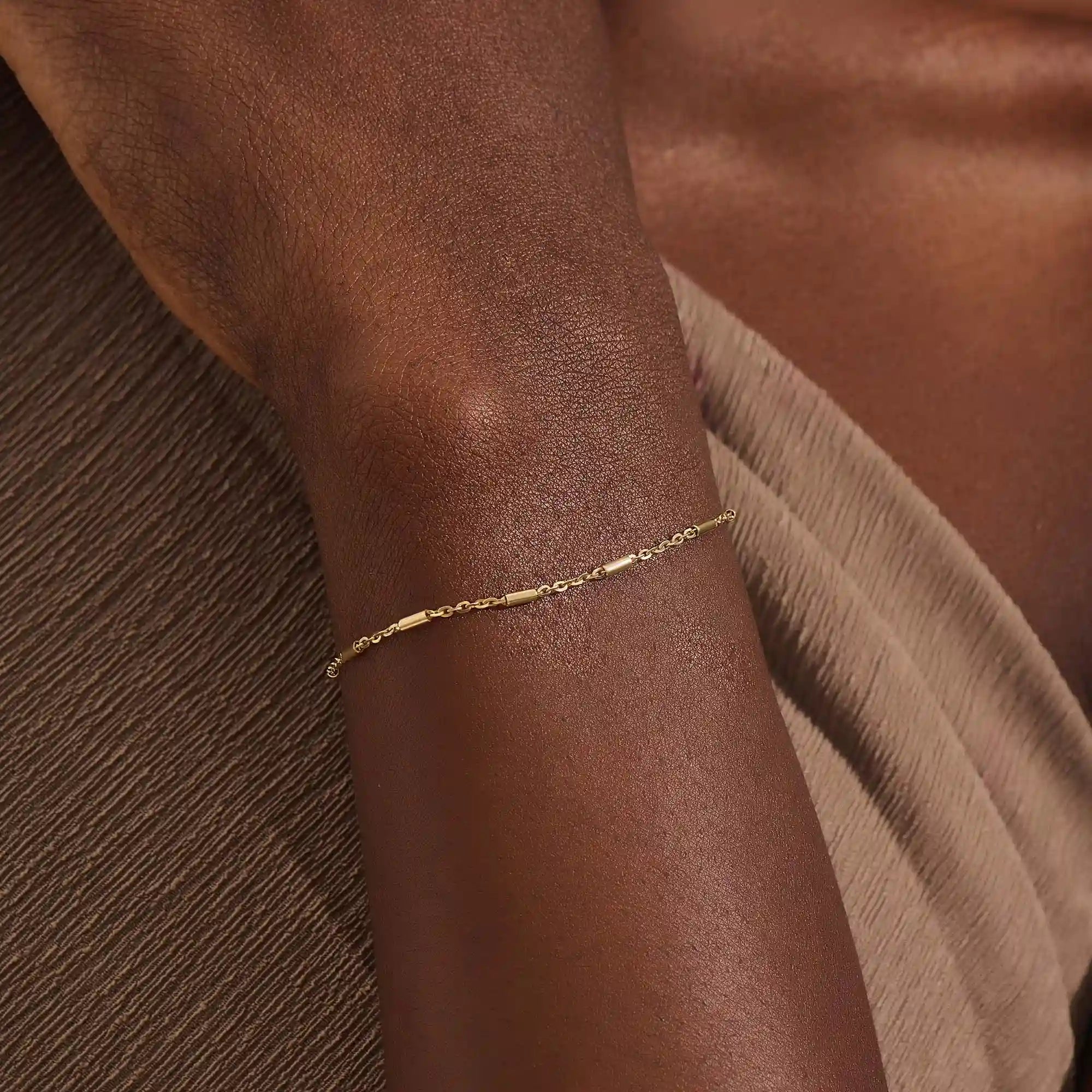 Close-up of a woman wearing a 14k solid yellow gold bar chain bracelet, its delicate design draping gracefully on the wrist for a refined everyday look.
