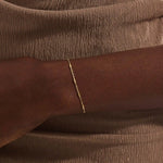 Close-up of a woman wearing a 14k solid yellow gold bar chain bracelet, its delicate design draping gracefully on the wrist for a refined everyday look.
