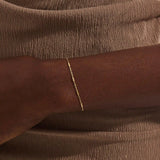 Close-up of a woman wearing a 14k solid yellow gold bar chain bracelet, its delicate design draping gracefully on the wrist for a refined everyday look.
