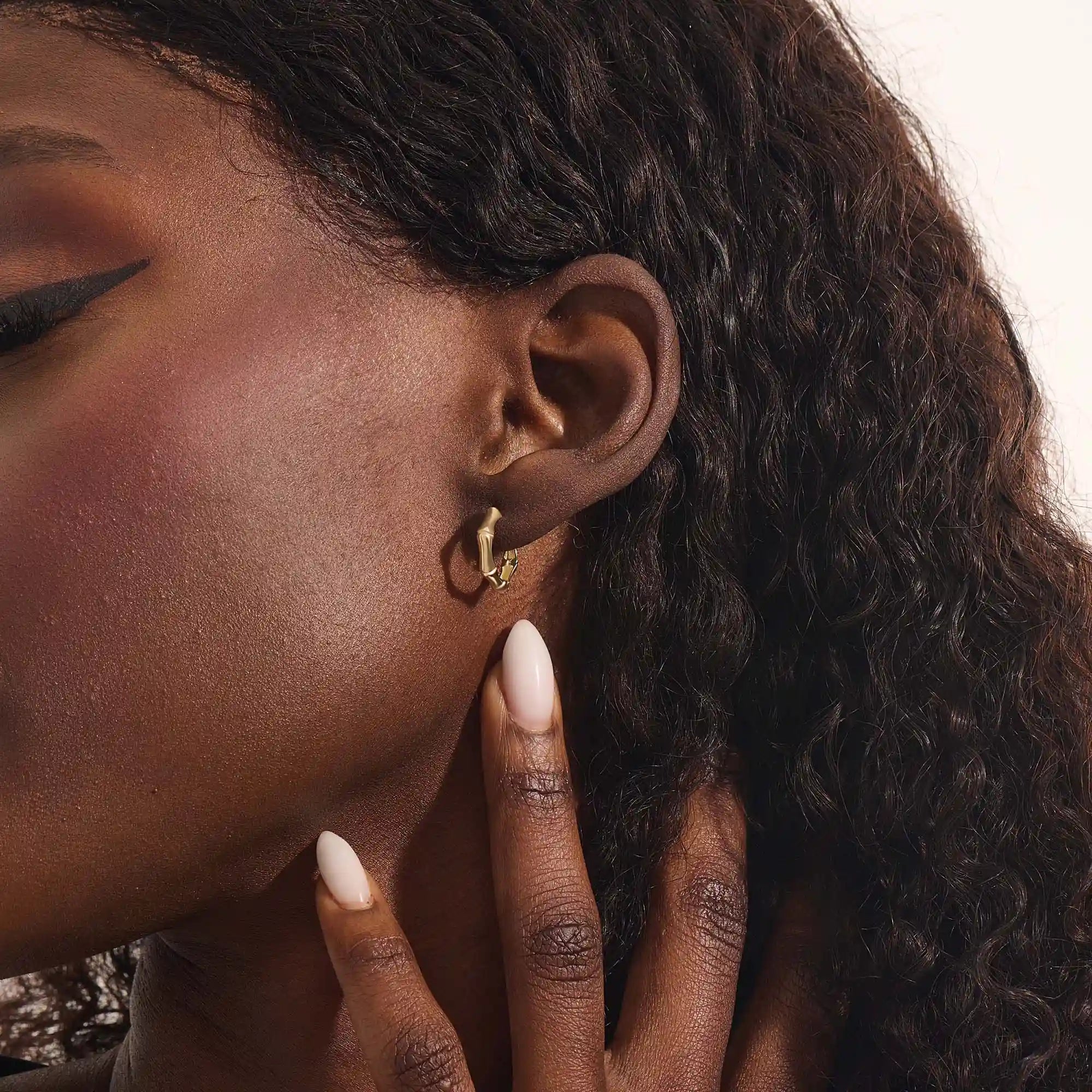 Close-up of a woman wearing a 14k solid yellow gold bone-style hoop earring, its organic curves and angular edges creating a modern, standout look.
