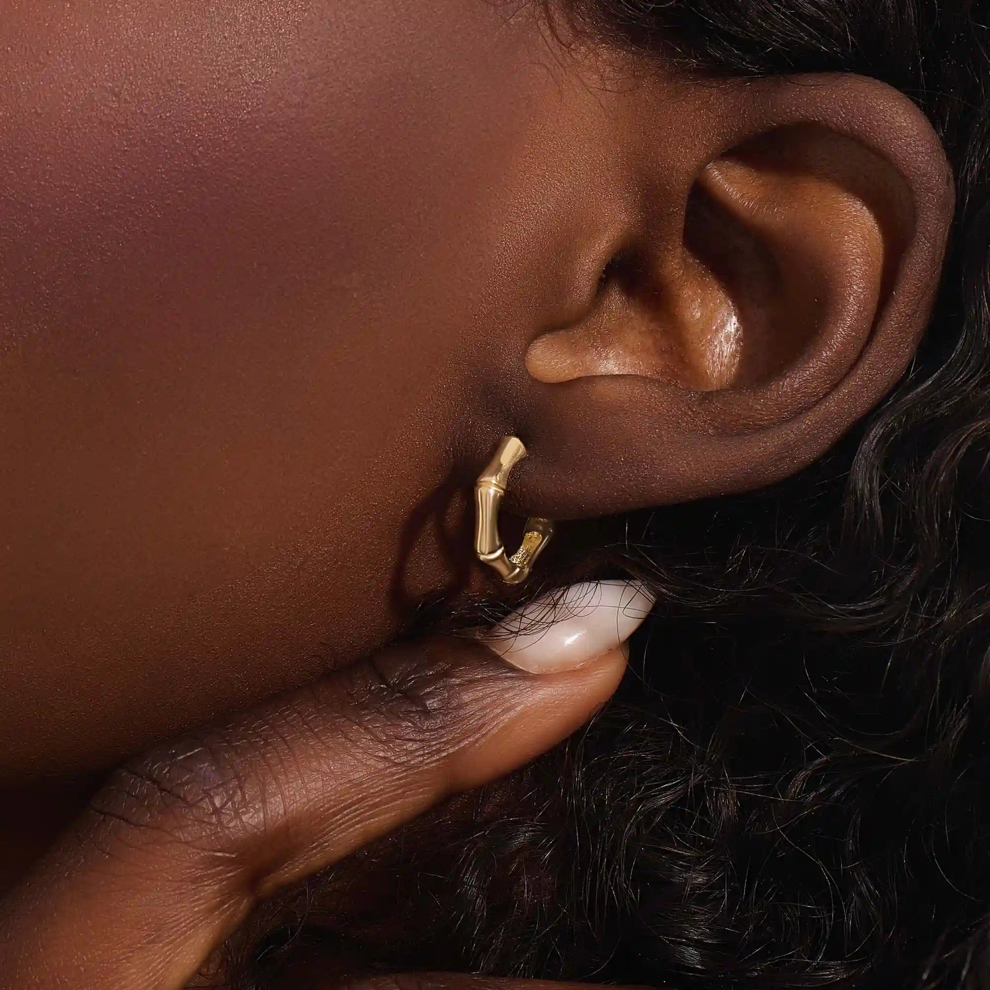 Close-up of a woman wearing a 14k solid yellow gold bone-style hoop earring, its organic curves and angular edges creating a modern, standout look.
