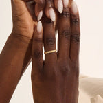 Close-up of a woman wearing a 14k solid yellow gold braided wedding band with a row of round diamonds, elegant and understated style
