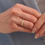 Close-up of a woman wearing a 14k solid yellow gold braided wedding band with a row of round diamonds, elegant and understated style
