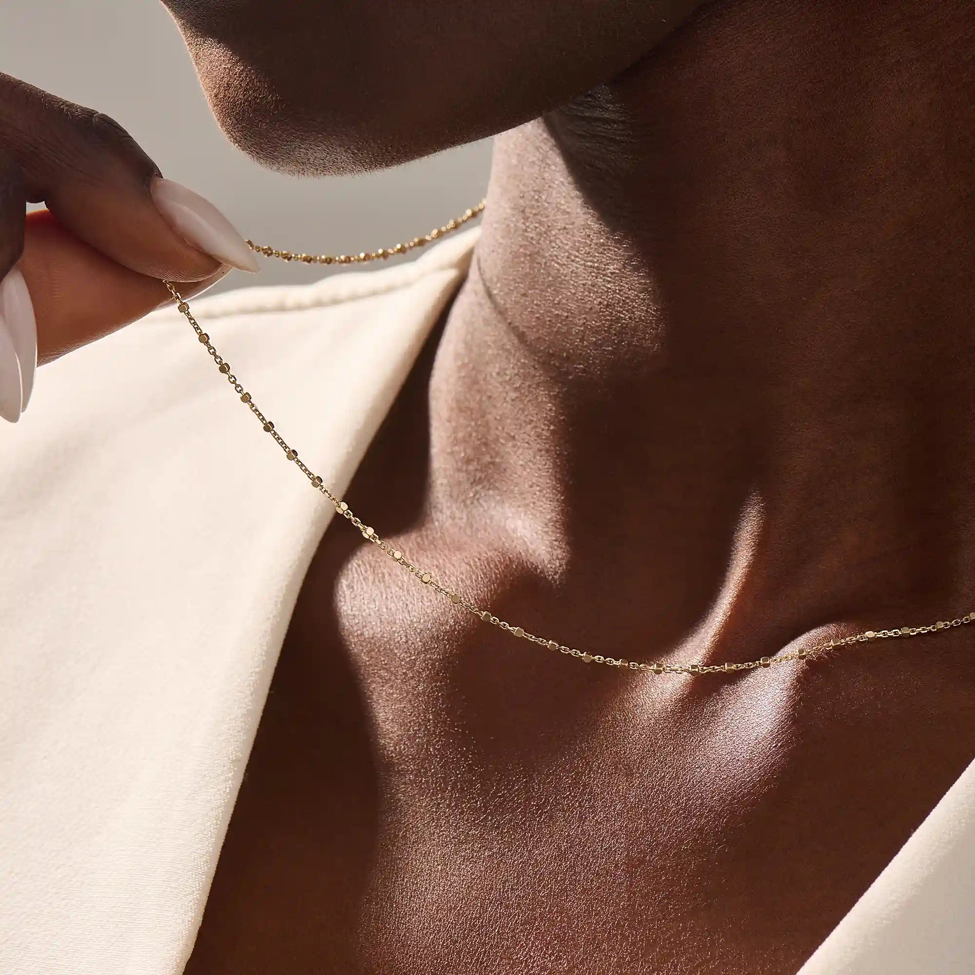 Close-up of a woman wearing a 14k solid yellow gold dot chain necklace with evenly spaced flat square links, styled alone for a simple, modern statement.
