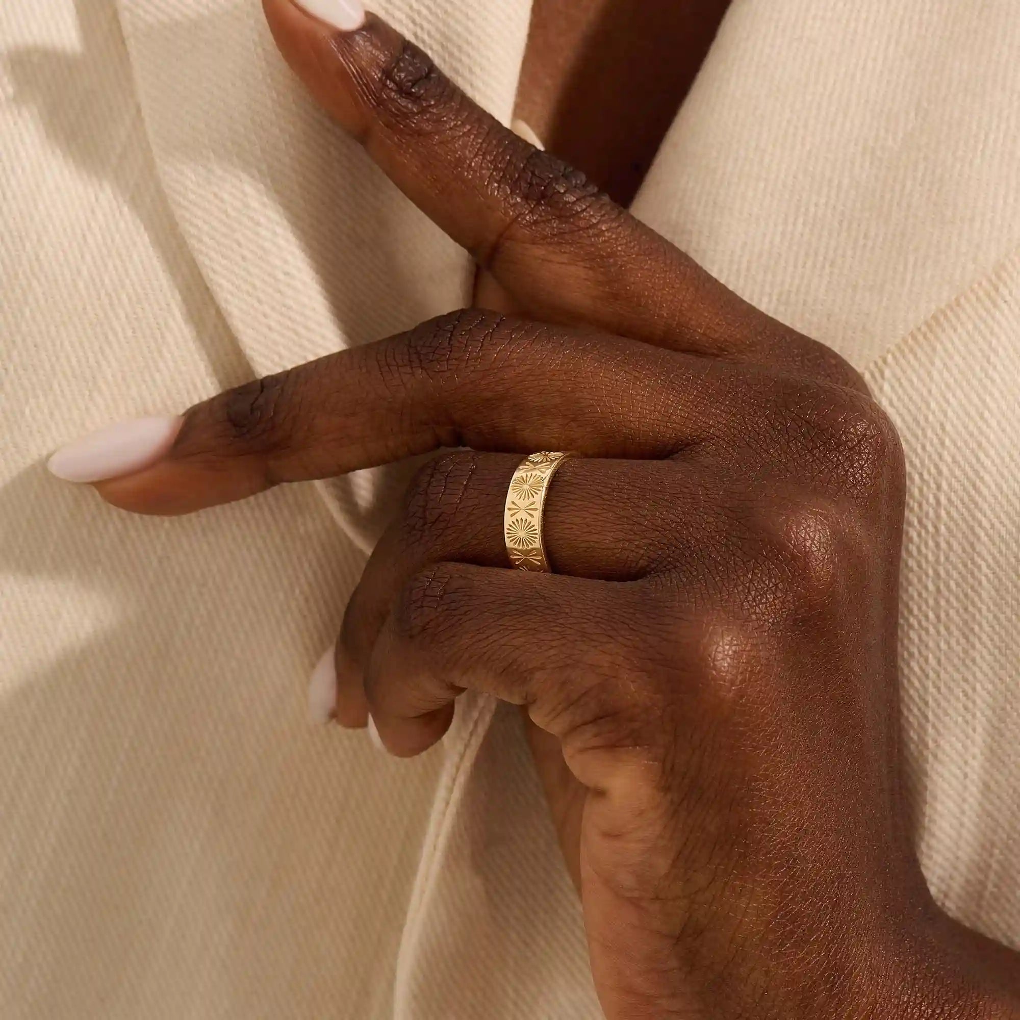 Close-up of a woman wearing a 14k solid yellow gold engraved floral wedding band with intricate detailing
