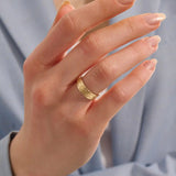 Close-up of a woman wearing a 14k solid yellow gold engraved floral wedding band with intricate detailing
