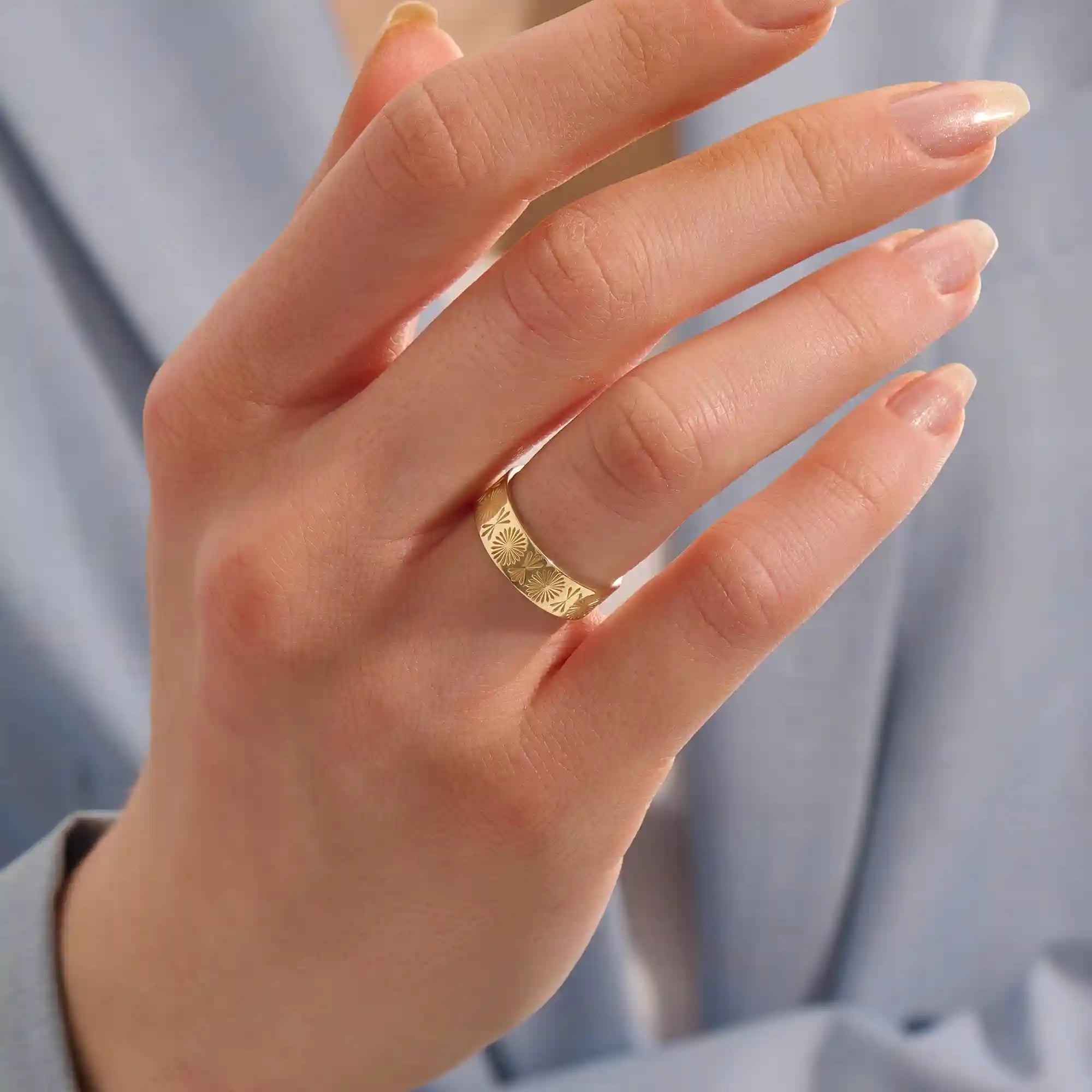Close-up of a woman wearing a 14k solid yellow gold engraved floral wedding band with intricate detailing
