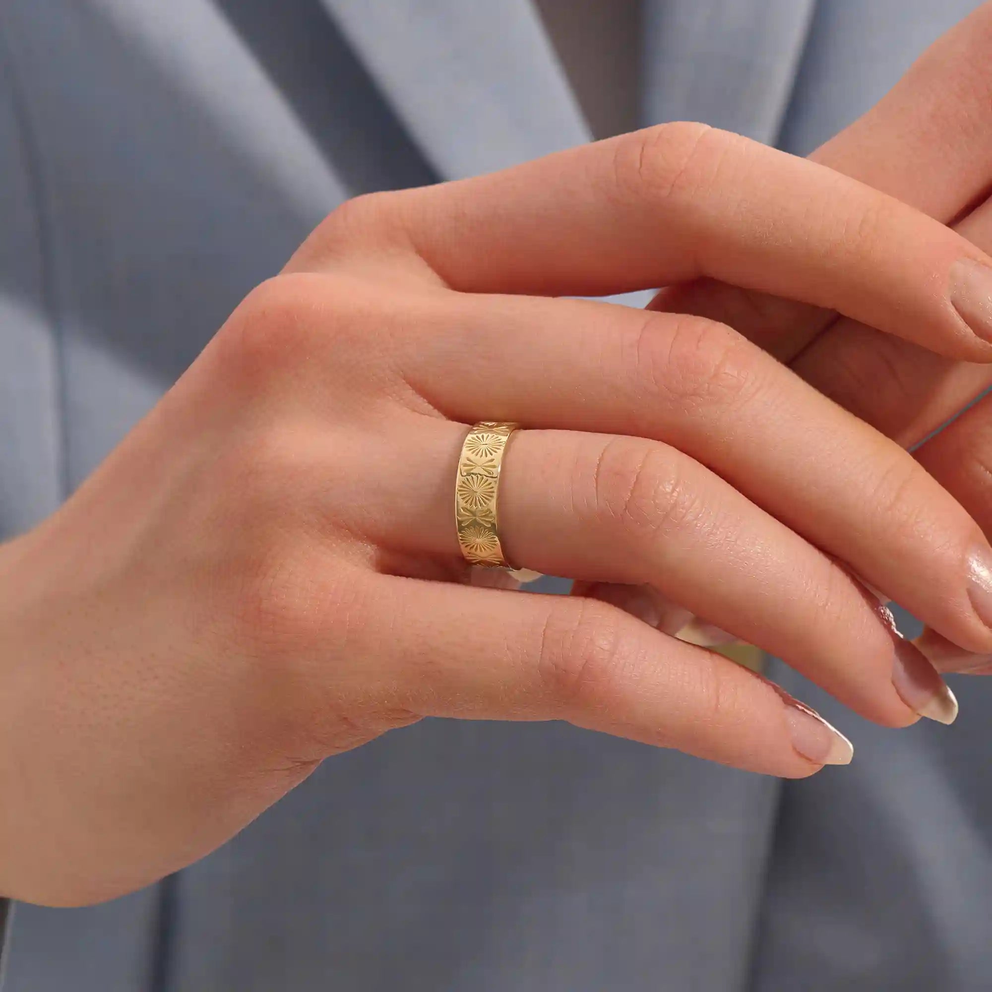Close-up of a woman wearing a 14k solid yellow gold engraved floral wedding band with intricate detailing
