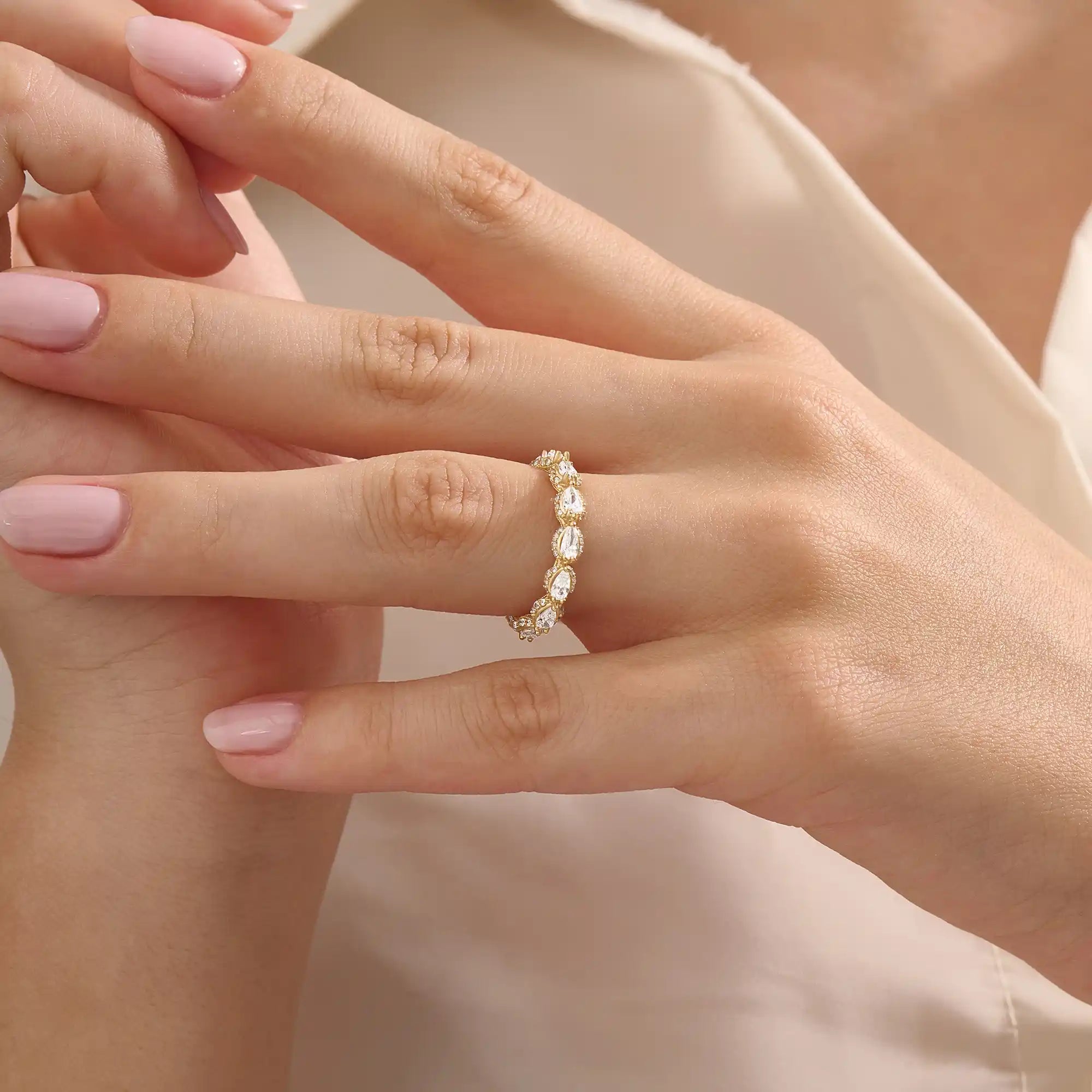 Close-up of a woman wearing a 14k solid yellow gold eternity band with sideways pear cut moissanite stones and pavé set round moissanite accents, ornate and elegant wedding jewelry
