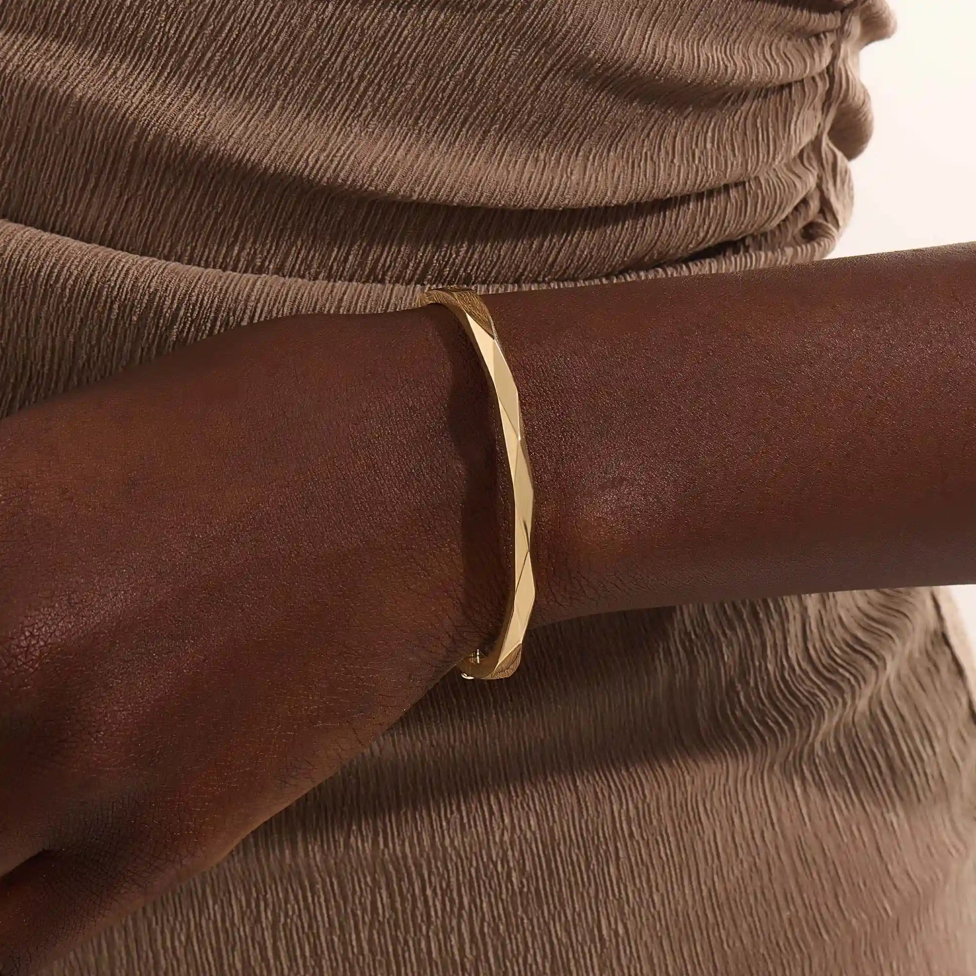 Close-up of a woman wearing a 14k solid yellow gold faceted bangle bracelet, showing the bracelet’s subtle geometric texture and reflective shine on the wrist.
