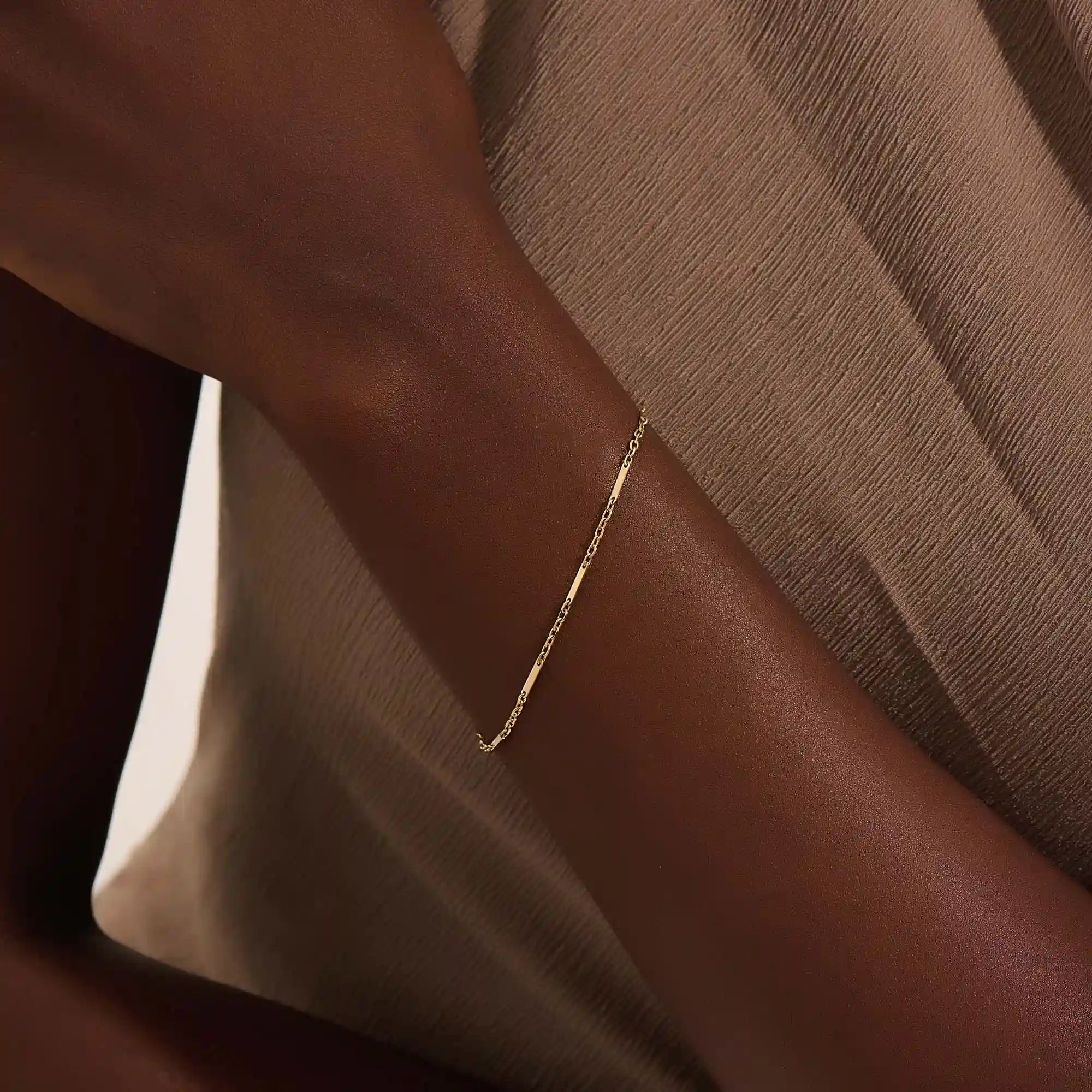 Close-up of a woman wearing a 14k solid yellow gold flat bar chain bracelet, the delicate design draping elegantly across the wrist for a timeless minimalist look.
