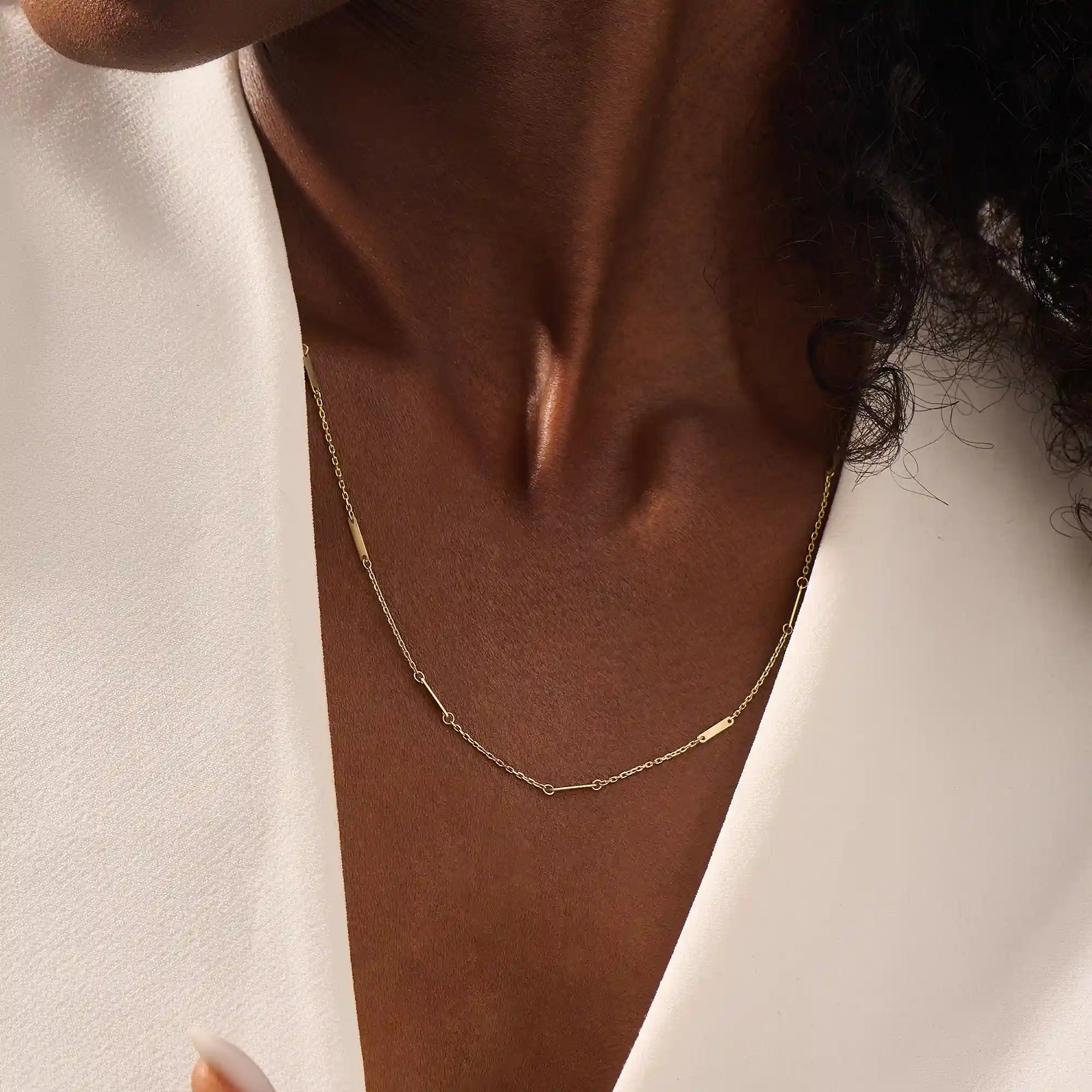 Close-up of a woman wearing a 14k solid yellow gold flat bar chain necklace with evenly spaced polished rectangular accents, styled alone for a refined, modern statement.
