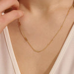 Close-up of a woman wearing a 14k solid yellow gold flat bar chain necklace with evenly spaced polished rectangular accents, styled alone for a refined, modern statement.

