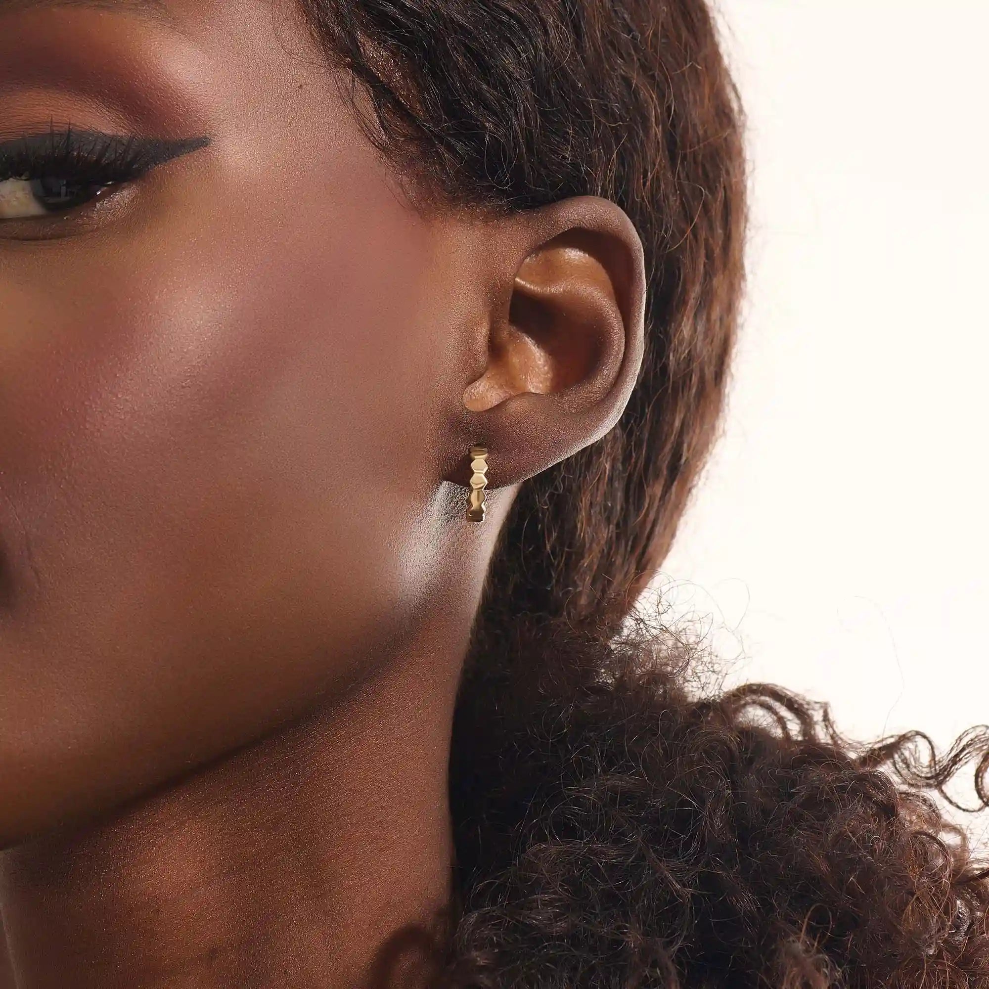Close-up of a woman wearing a 14k solid yellow gold hexagon hoop earring, its geometric links catching the light with each movement.
