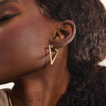 Close-up of a woman wearing a 14k solid yellow gold open triangle hoop earring, its minimalist geometric form making a bold modern statement.
