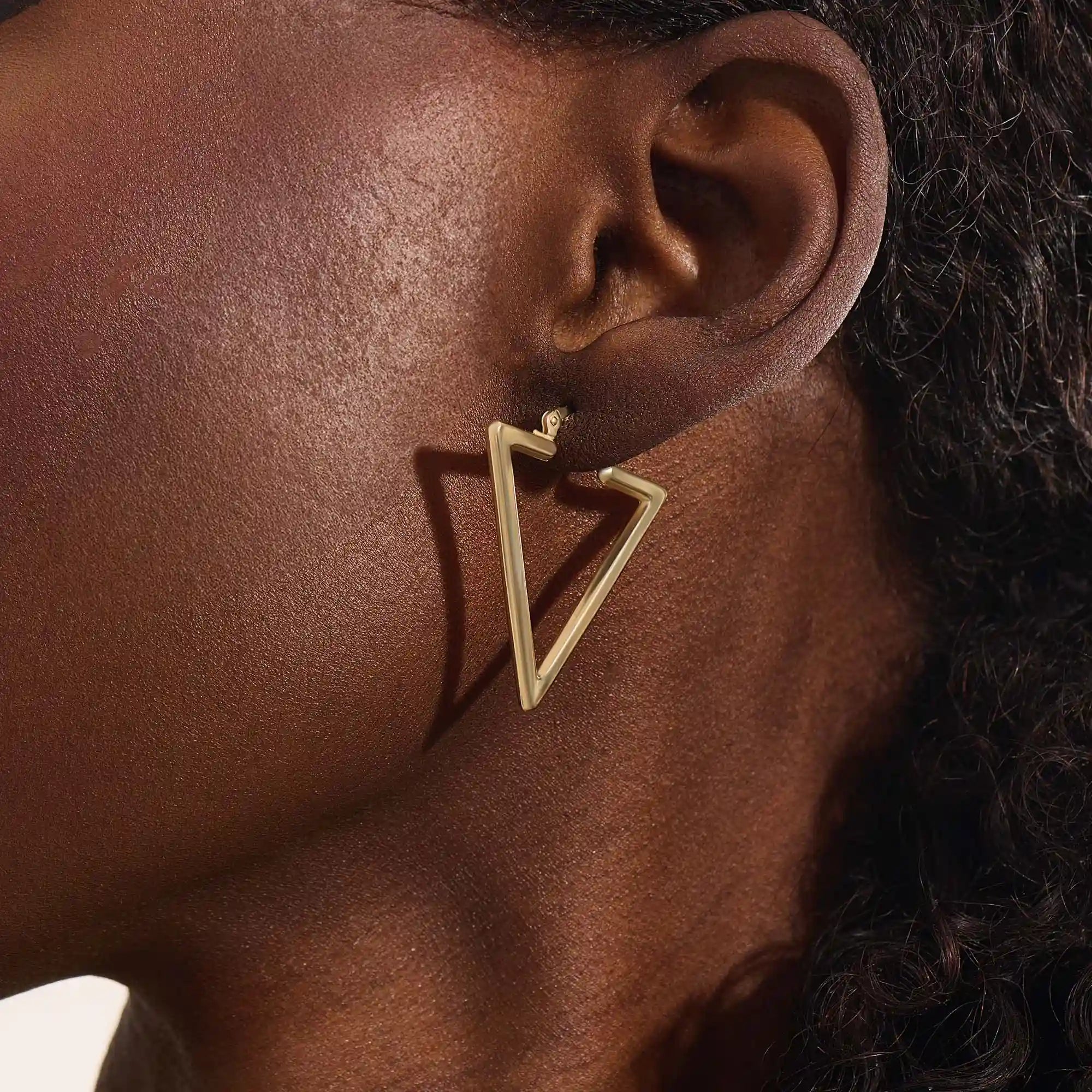 Close-up of a woman wearing a 14k solid yellow gold open triangle hoop earring, its minimalist geometric form making a bold modern statement.
