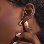 Close-up of a woman wearing a 14k solid yellow gold rope half hoop stud, the pavé white moissanite stones catching the light against the rope-like texture.
